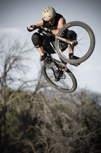 Mountain biker jumping off dirt ramps.